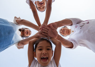 Low angle view of family stacking hands against clear sky