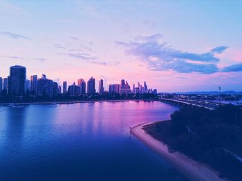 Scenic view of river by buildings against sky at sunset