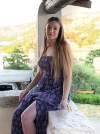 Portrait of beautiful young woman sitting on retaining wall