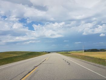 Empty road amidst field against sky