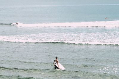 Man with surfboard walking in sea against sky