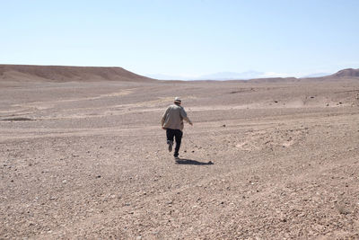 Rear view of man running in desert against clear sky