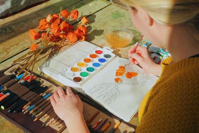Midsection of female artist painting flowers in notebook