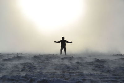 Silhouette man with arms outstretched standing on fog against sky