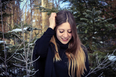 Portrait of smiling young woman standing against trees