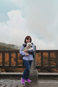 Portrait of woman with dog standing by railing against sky