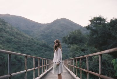 Young woman standing on footbridge against mountain