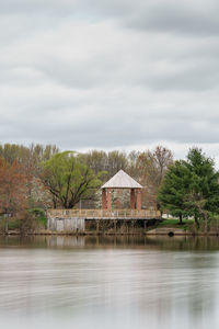 House by lake and trees against sky