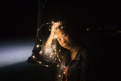 Portrait of woman holding illuminated lighting equipment at night