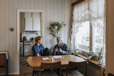 Senior man discussing with female caregiver while sitting at dining table in home