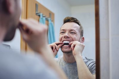 Young man preparing silicon tray for teeth whitening with bleaching gel.