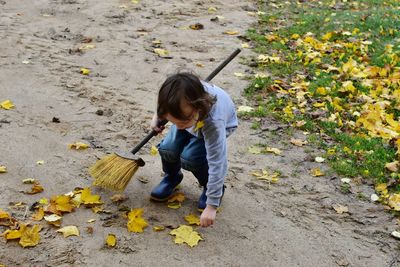 High angle view of boy holding broom and autumn leaves