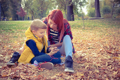 Mother with son using smart phone while sitting on field at park during autumn