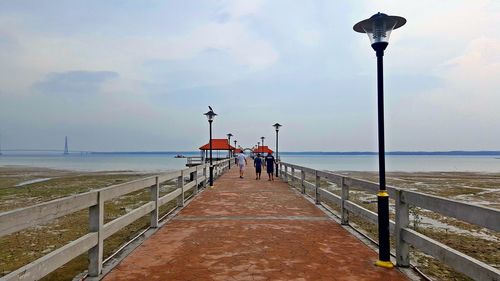 Rear view of people on street by sea against sky