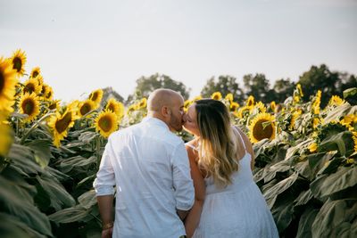 Rear view of friends standing on flowering plants against sky