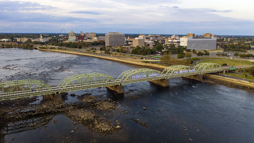 Bridge over river by buildings in city against sky