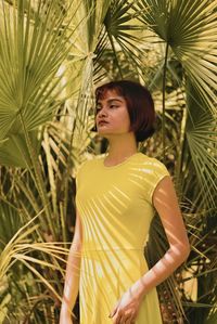 Young woman looking away while standing against plants