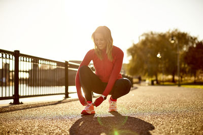 A female runner ties her sneaker on a path in a city park.