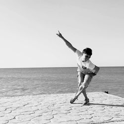 Full length of man dancing on pier at sea against clear sky