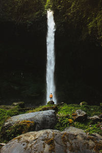 Mid distance view of teenage boy standing by waterfall in forest