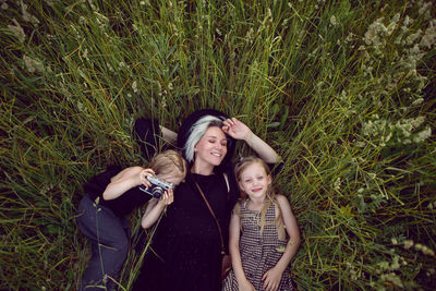 Mother in evening dress and retro camera with two daughters lying, green field with grass in summer