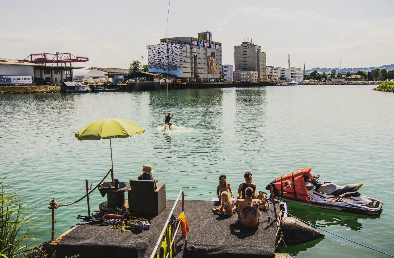 water, architecture, built structure, real people, group of people, building exterior, men, transportation, day, lifestyles, nature, sitting, nautical vessel, mode of transportation, group, sky, river, medium group of people, city, outdoors