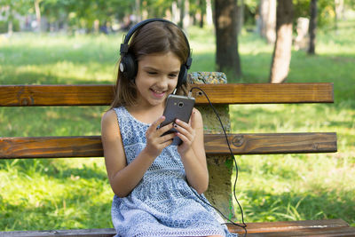 Smiling girl listening music while sitting on bench at park