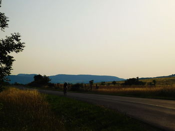 Road by field against clear sky during sunset