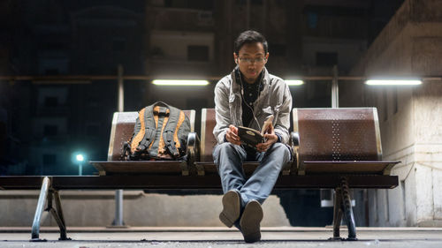 Full length of man reading book while sitting at railroad station platform