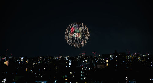 Firework display in city against sky at night