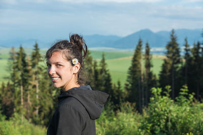 Side view portrait of smiling young woman wearing flower in forest