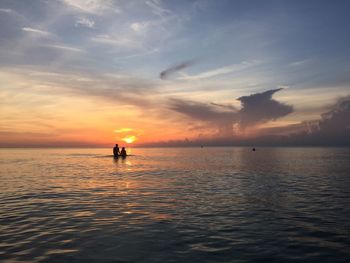 Silhouette couple amidst sea against sky during sunrise