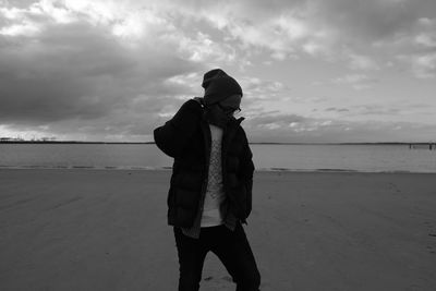 Young man standing at beach against cloudy sky