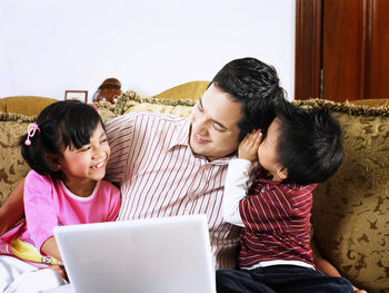 Father with children using laptop on sofa at home
