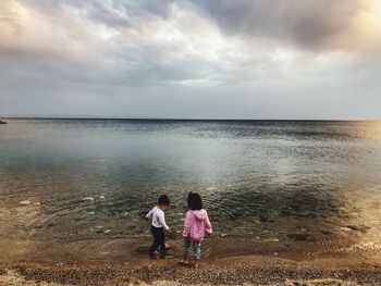 Siblings playing at beach against sky