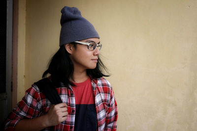 Young woman looking away while standing against wall