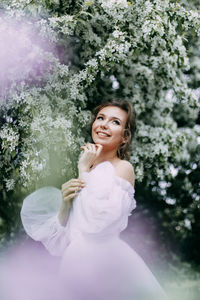 Beautiful bride in a wedding dress walks in a blooming apple-tree park in spring