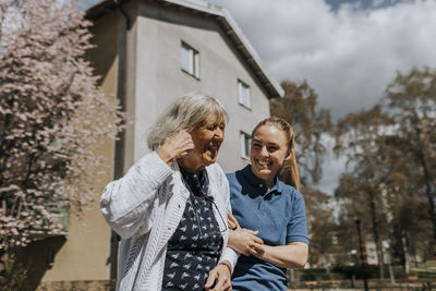 Happy female caregiver with arm in arm of senior woman during sunny day