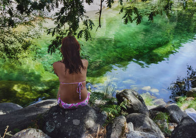 Rear view of bikini woman sitting on rock by stream