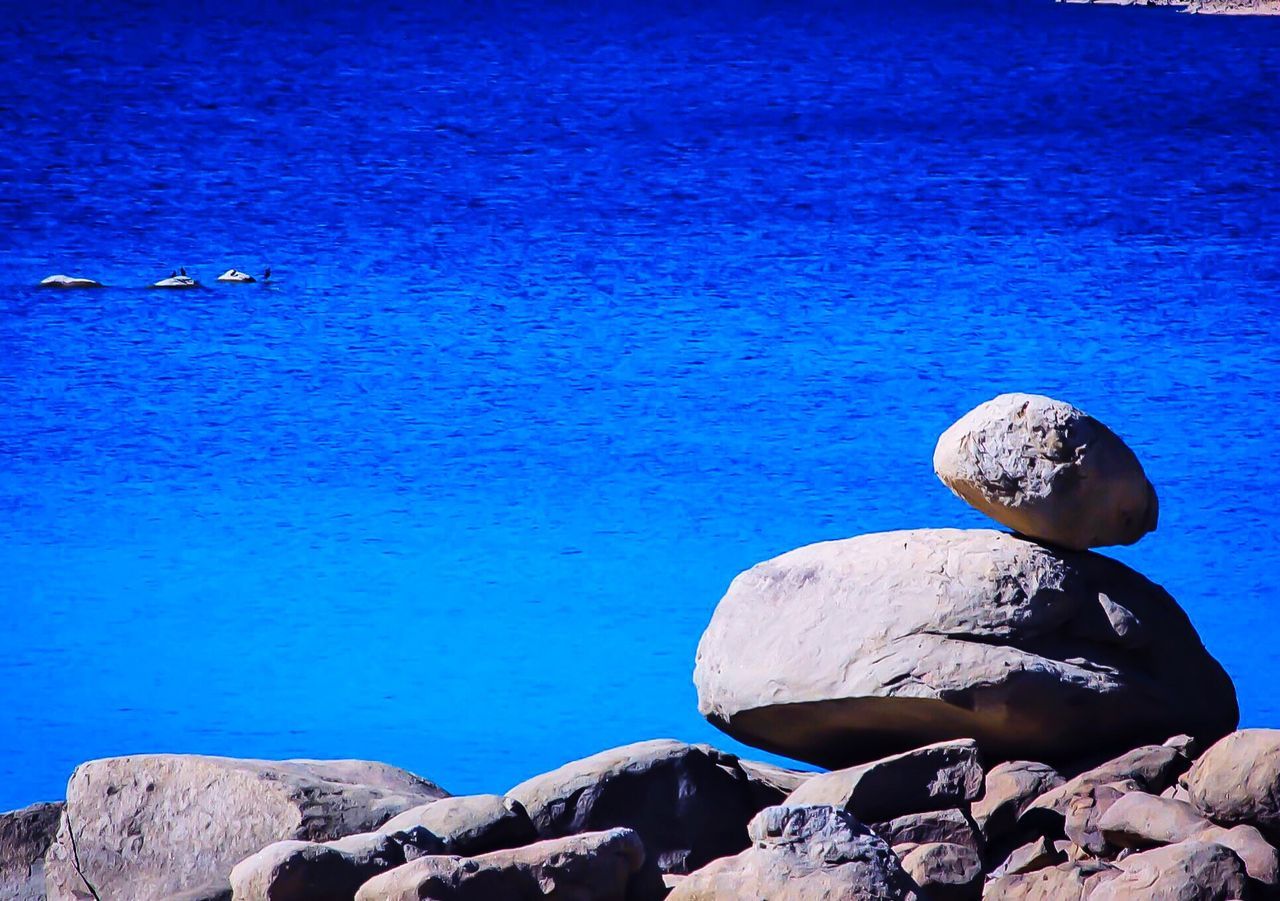 blue, rock - object, water, sea, rock, tranquility, stone - object, nature, beauty in nature, tranquil scene, scenics, stone, clear sky, rock formation, sunlight, day, no people, outdoors, pebble, copy space