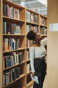 Female student searching books on shelf in library at university