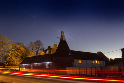 Light trails on road amidst buildings against sky at night