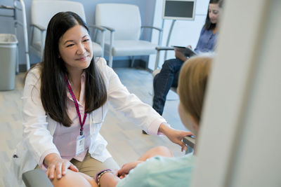 High angle view of pediatrician talking with patient while woman using tablet computer in background