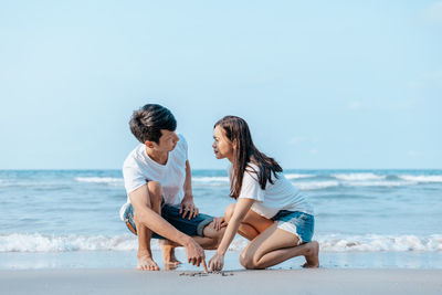 Friends sitting on beach against sea