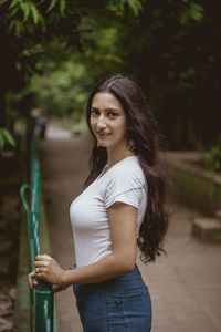 Portrait of smiling woman standing by railing against tree