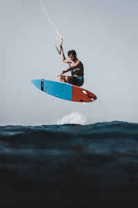 Side view of man kiteboarding in sea against clear sky