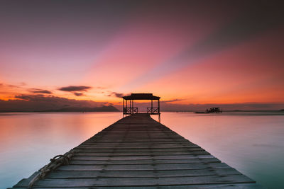 Pier over lake against orange sky