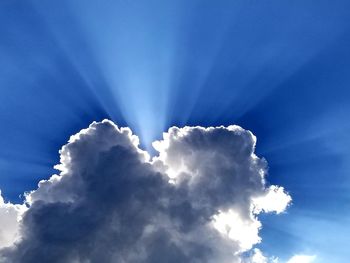 Low angle view of sunlight streaming through clouds