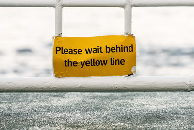 Yellow sign that says please wait begind the yellow line
