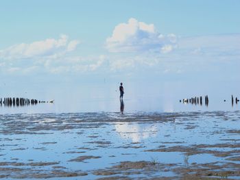 Man standing on shore at beach against sky